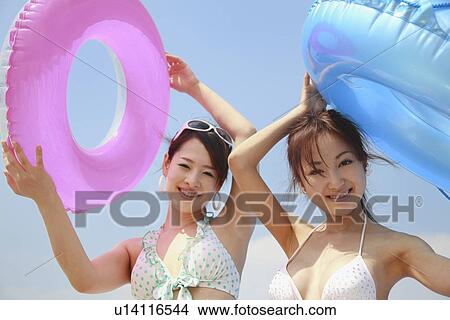 Picture - Two young women in bikini holding inner tube. Fotosearch