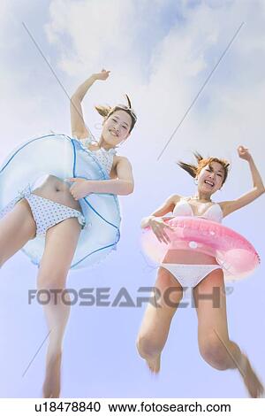 Stock Image - Two young women in bikini jumping. Fotosearch