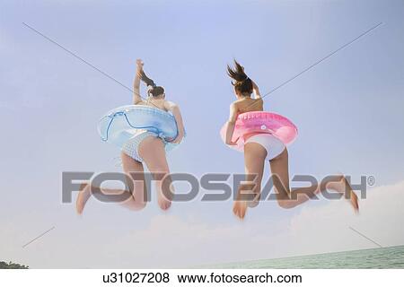 Stock Photo - Two young women in bikini jumping. Fotosearch