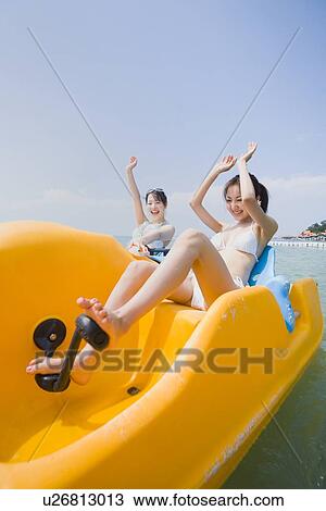 Stock Image - Two young women riding on pedal boat. Fotosearch