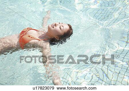 Stock Photo - Young woman floating in pool. Fotosearch