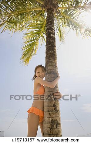 Stock Photo - Young woman in bikini holding palm tree. Fotosearch