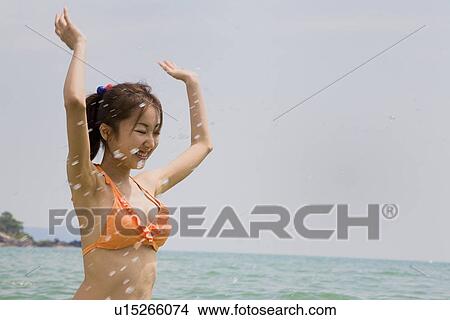 Picture - Young woman in bikini splashing water. Fotosearch
