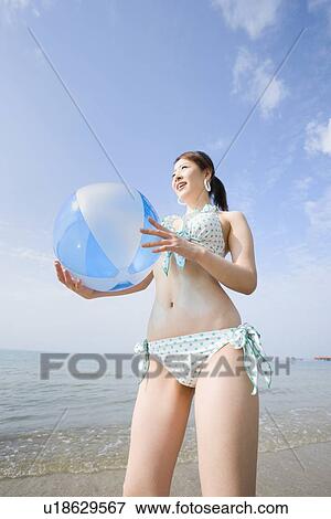 Stock Photo - Young woman standing with beach ball. Fotosearch