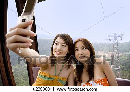 Two young women photographing with mobile phone View Large Photo Image Stock Image - Two young women photographing with mobile phone. Fotosearch