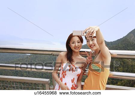 Stock Photo - Two young women photographing with mobile phone. Fotosearch