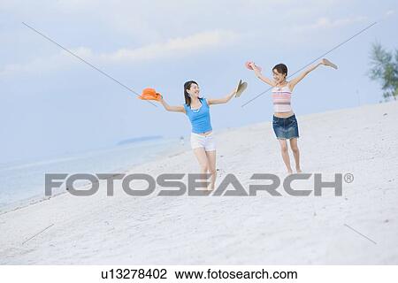 Stock Image - Two young women walking at beach. Fotosearch