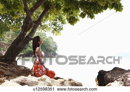 Stock Image - Young woman sitting at beach. Fotosearch