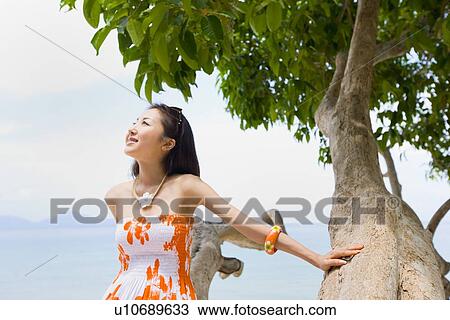 Stock Image - Young woman sitting on tree. Fotosearch