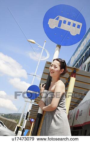 Stock Photo - Young woman standing at bus stop. Fotosearch
