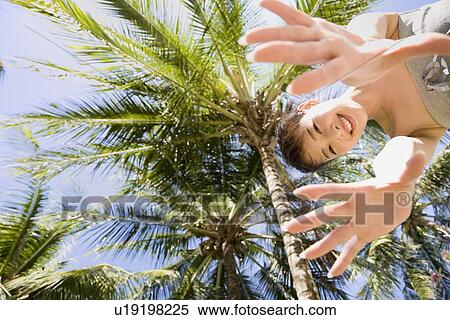 Stock Photography - Young woman standing by palm tree. Fotosearch