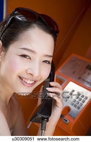 Stock Image - Young woman using public phone. Fotosearch