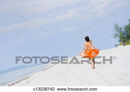 Stock Image - Young woman walking at beach. Fotosearch