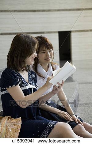 Stock Image - Two young women looking at book. Fotosearch