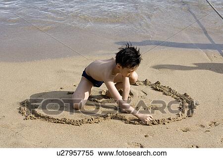 Stock Photography - A boy is drawing a heart shape on the sand. Fotosearch