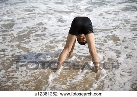 Stock Image - A boy standing in water with headstand. Fotosearch