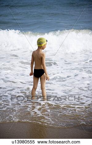 Stock Photography - A little boy standing in water and looking at the sea. Fotosearch