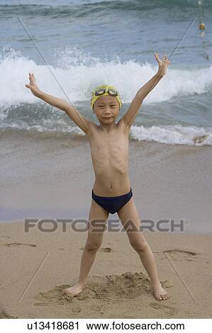 Stock Image - A little boy standing on the sand with arms outstretched. Fotosearch