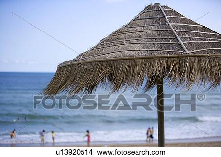 Picture - A thatched sunshade and some people playing on the seaside. Fotosearch