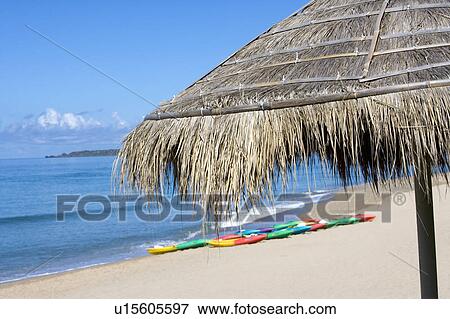 Stock Photo - A thatched sunshade and two multicolored boats beside the sea. Fotosearch