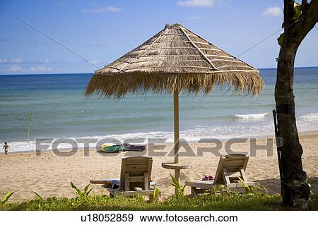 Stock Photo - A thatched sunshade and two wooden longue chairs at beach. Fotosearch