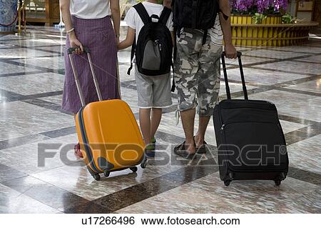 Stock Photograph - A women and a man pulling the suitcase with their child, lower section. Fotosearch