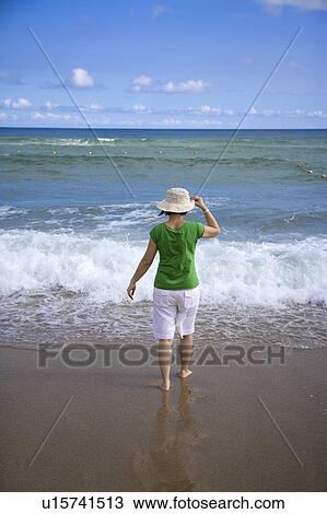 Stock Image - A women is standing on the sand and walking towards the beach. Fotosearch