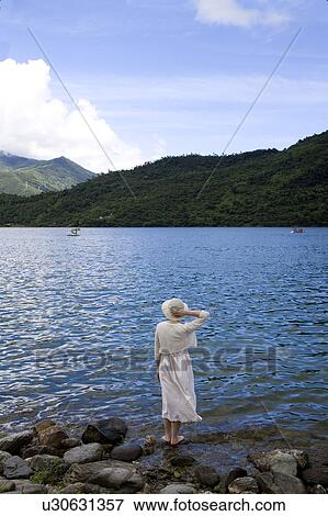 Stock Photo - A women standing on the rock, looking at the lake. Fotosearch