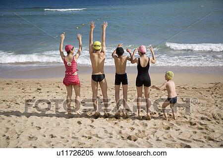 Stock Photography - Five children standing on the sand with arms outstretched. Fotosearch