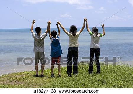 Four people standing on the hill toward the sea and holding hands together View Large Photo Image Stock Photo - Four people standing on the hill toward the sea and holding hands together. Fotosearch