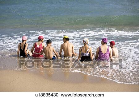 Stock Image - Seven people sitting in the water on the beach. Fotosearch