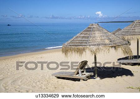 Sunshades of thatched roof and a wooden longue chair at beach View Large Photo Image Stock Photo - Sunshades of thatched roof and a wooden longue chair at beach. Fotosearch