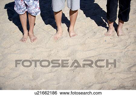 Three people standing on the sand, lower section View Large Photo Image Stock Photograph - Three people standing on the sand, lower section. Fotosearch