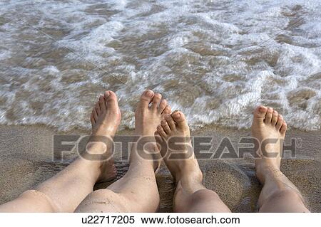 Stock Photography - Two people lying on sand beside the sea, lower section. Fotosearch