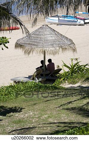 Two person sitting under a sunshade at beach View Large Photo Image Stock Image - Two person sitting under a sunshade at beach. Fotosearch