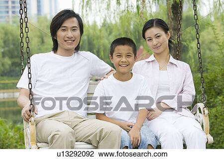 Stock Image - Family with son sitting on the glider and looking at the camera. Fotosearch