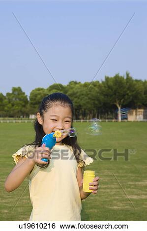 Stock Photograph - Little girl blowing bubbles and smiling happily. Fotosearch