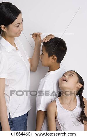 Stock Image - Mother measuring the height of two children. Fotosearch