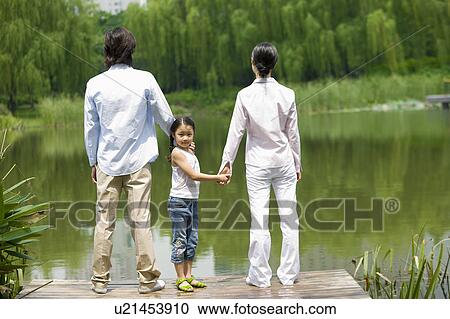 Stock Image - Young family with daughter standing at the lakeside. Fotosearch