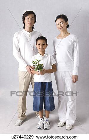 Stock Photo - Young family with son standing together and holding potted plant. Fotosearch