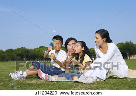 Stock Image - Young family with two children blowing bubbles on the lawn. Fotosearch
