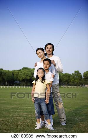 Stock Photography - Young family with two children standing closely on the lawn. Fotosearch