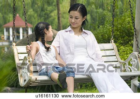 Young mother and daughter sitting on the glider and looking at each other View Large Photo Image Stock Image - Young mother and daughter sitting on the glider and looking at each other. Fotosearch