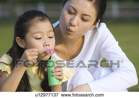 Stock Photo - Young mother with daughter blowing bubbles together. Fotosearch