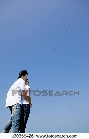 Young couple bonding together against clear sky View Large Photo Image Stock Photograph - Young couple bonding together against clear sky. Fotosearch