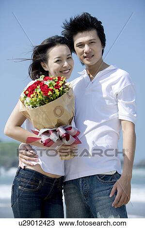 Stock Image - Young couple bonding together and holding a bunch of flowers. Fotosearch