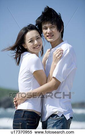 Stock Photography - Young couple bonding together at beach and looking at the camera. Fotosearch