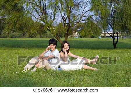 Young couple sitting on the lawn and on the phone, back to back View Large Photo Image Stock Image - Young couple sitting on the lawn and on the phone, back to back. Fotosearch