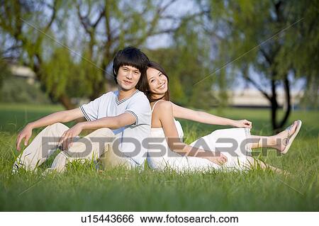 Stock Photograph - Young couple sitting on the lawn, back to back. Fotosearch