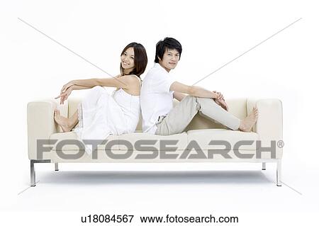 Stock Photo - Young couple sitting on the sofa, back to back. Fotosearch